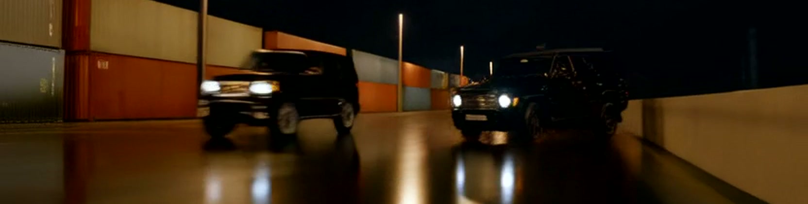 Two black SUVs on a wet road at night